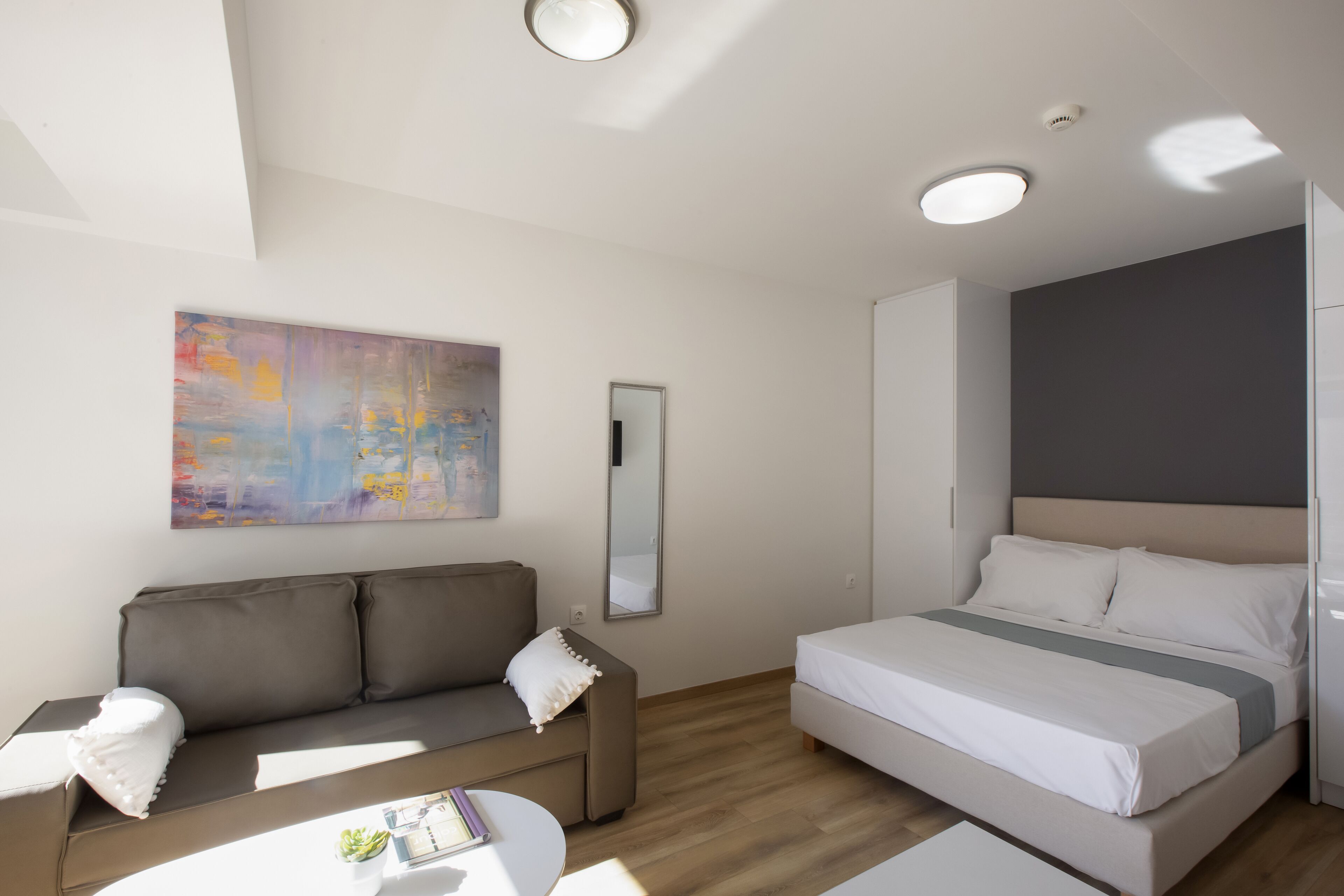 A modern hotel room with a sofa, a bed, a small table, and a painting on the wall.