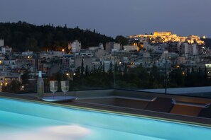 Terraza en la azotea con vista a la ciudad, dos copas de vino y una botella sobre la mesa.
