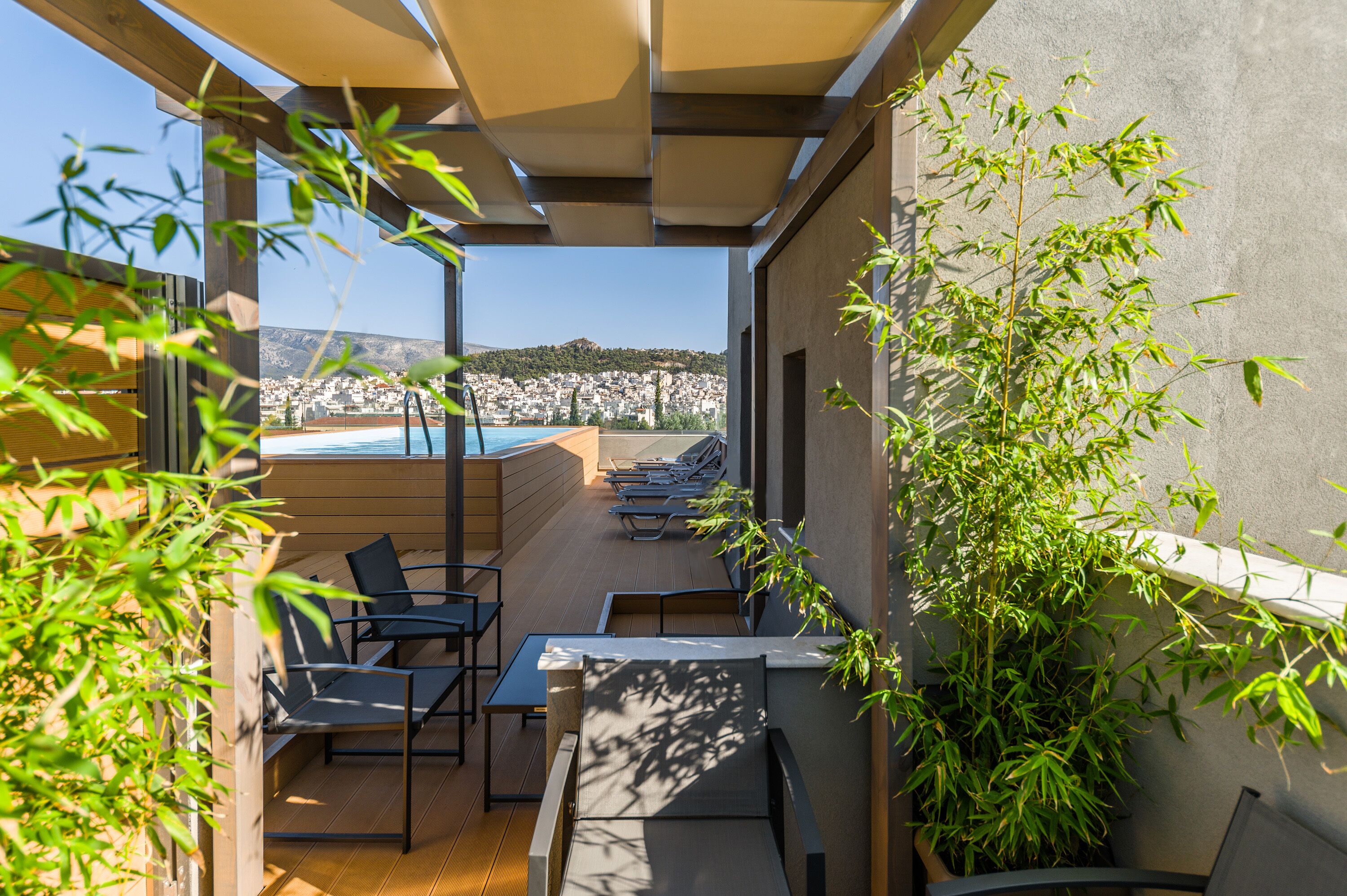 A rooftop terrace with outdoor seating, a pool, and a view of a hillside town.