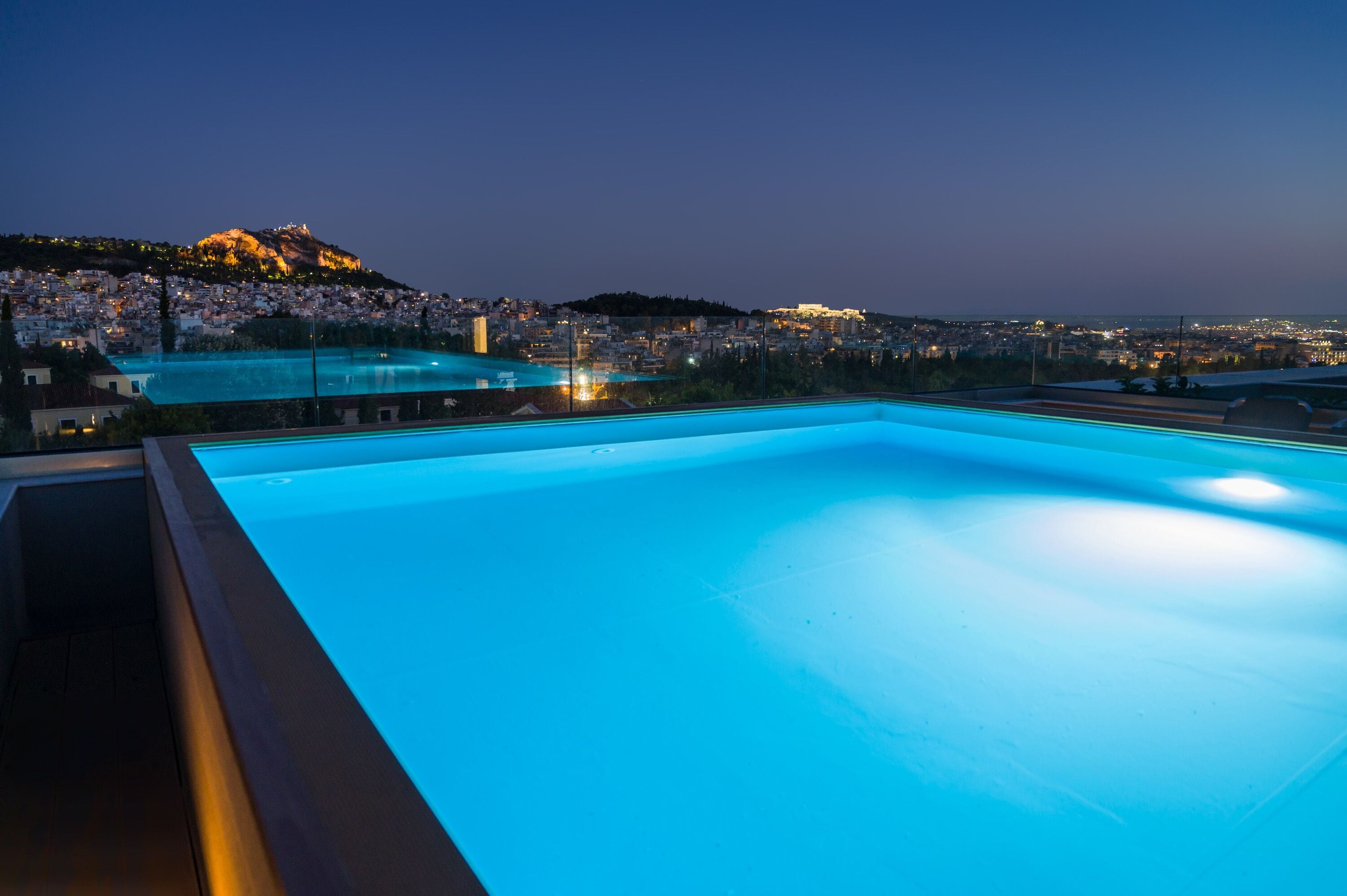 Piscina con vistas a un paisaje urbano y una colina al atardecer.