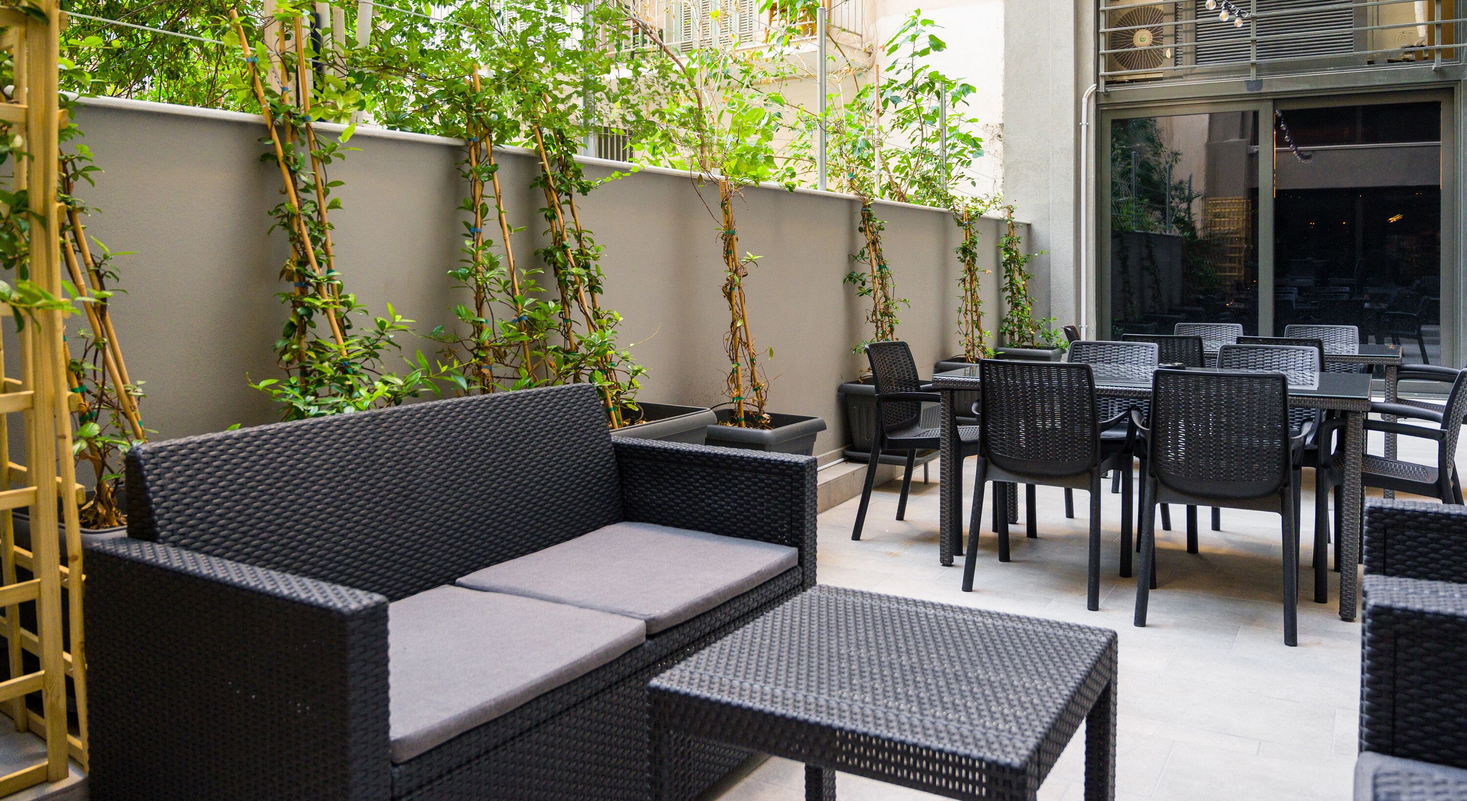 Un espace extérieur aménagé avec des meubles en osier, des plantes en pot et une vue sur la rue.