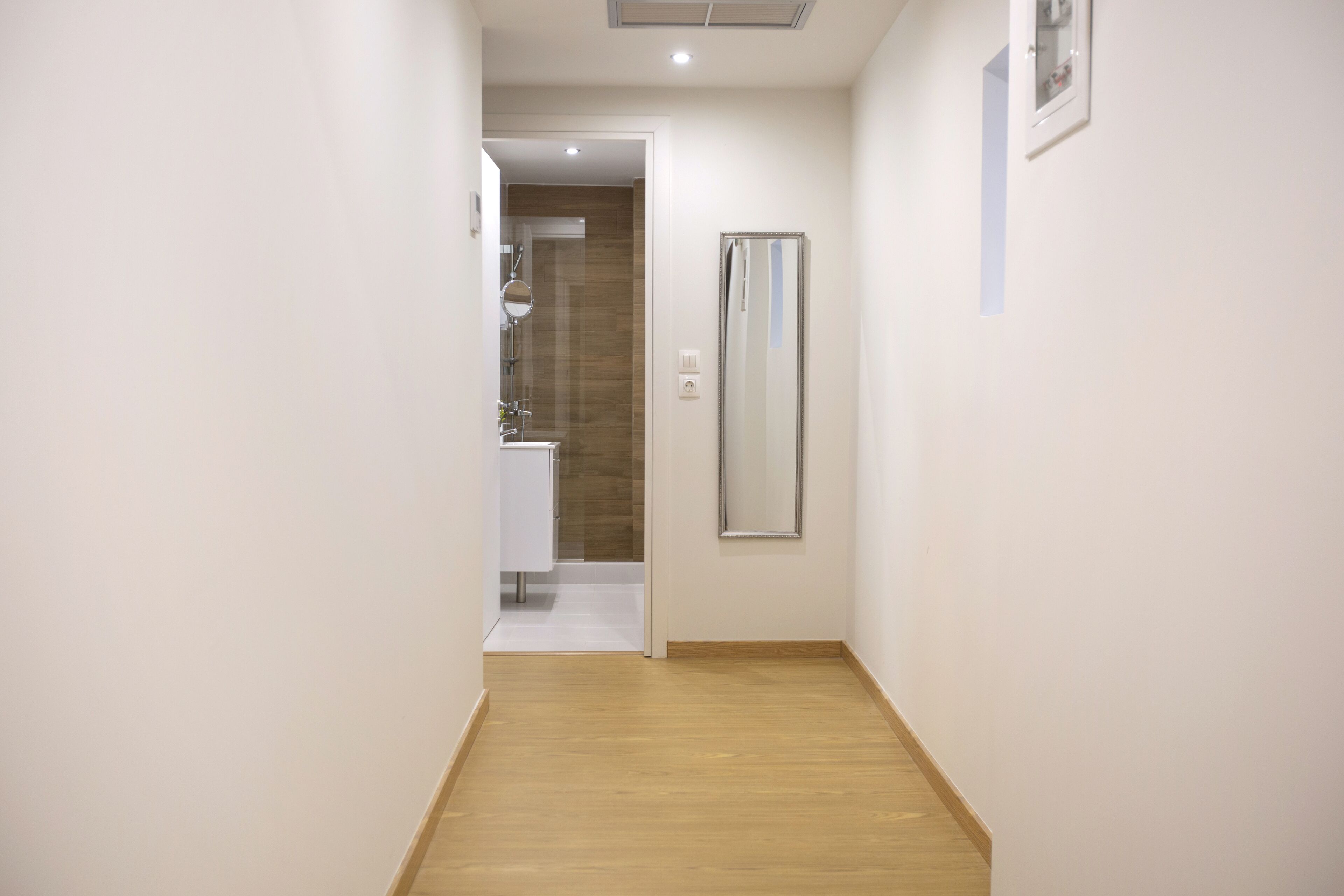 A narrow hallway with wooden flooring leading to a bathroom.