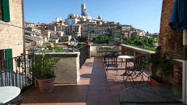 Terraza en la azotea con mobiliario exterior, con vistas a un centro histórico donde destaca una torre de iglesia.