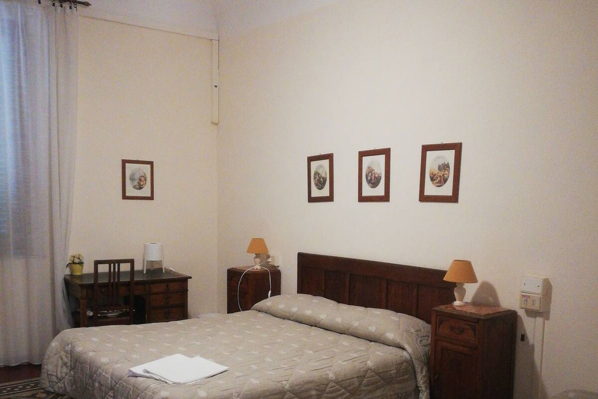 Une chambre d’hôtel avec un lit, un bureau, une chaise, une table de chevet et une lampe.