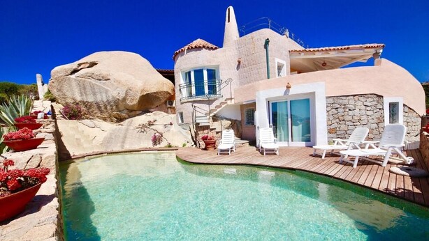 Una villa con piscina, mobiliario exterior y fachada de piedra.