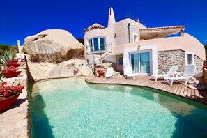 Eine Villa mit Swimmingpool, Sitzgelegenheiten im Freien und einer Steinfassade.