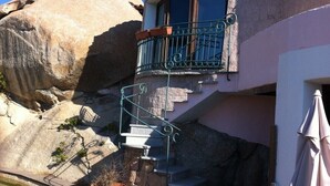 Un edificio de piedra con un balcón, escalones que conducen a la entrada y una gran roca cerca.