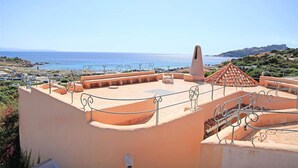 Una terraza en la azotea con vistas despejadas al mar, una estructura de piedra y un techo de tejas.