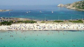 Una playa con aguas turquesas cristalinas, embarcaciones y una orilla arenosa con sombrillas.