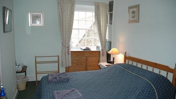 A bedroom with a bed, a wooden dresser, a chair, a window with curtains, and a lamp.