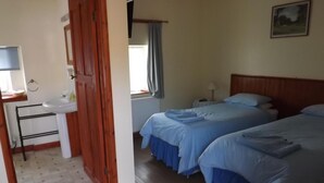 A bedroom with two beds, a wooden door, a sink, and a window with curtains. - Pear Tree Farm B&B (Kettering)