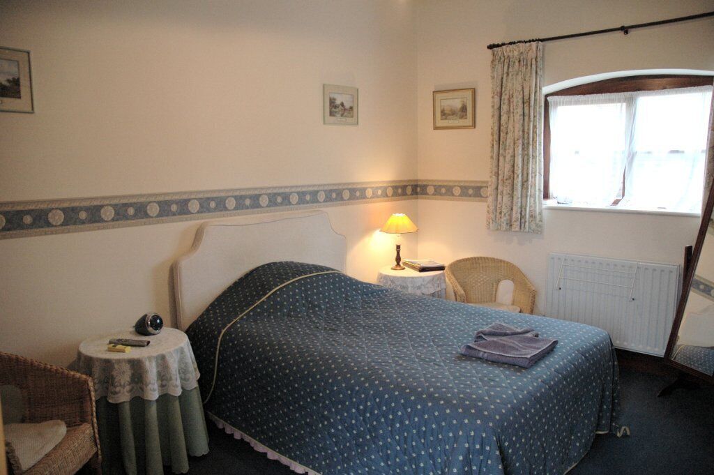 Een slaapkamer met een bed, nachtkastje met lamp, een stoel en een raam met gordijnen.