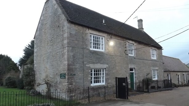 A stone building with a pitched roof, a green door, and a small fenced yard. - Pear Tree Farm B&B (Kettering)