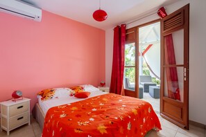 Un dormitorio con cama, mesita de noche, lámpara roja y puerta corrediza de vidrio que da a un espacio al aire libre.