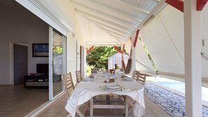 A dining area with a table set for six, a sliding glass door leading to a pool, and a view of a backyard with a wooden fence and greenery.