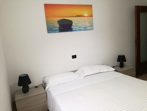 A bedroom with a bed, two bedside lamps, a nightstand, and a wall-mounted picture of a sunset over water. - Blue Sea Apartment CITRA 011017-LT-0579 CIN IT011017C2AS5ZOD4D (Levanto)
