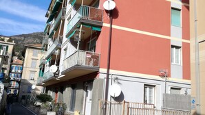 A multi-story building with balconies, satellite dishes, and a street in front.