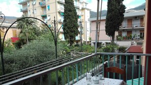 A balcony with a table set for two, overlooking a garden and residential buildings.