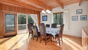 Comedor con mesa y sillas de madera, ventanas amplias y techo con vigas a la vista.