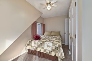 Een slaapkamer met een schuine plafond, een bed met een quilt met herten, een plafondventilator en een deur met een messing handvat.
