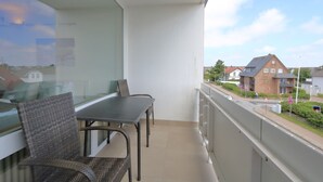 Ein Balkon mit Tisch und Stühlen, ein Fenster und Blick auf Häuser und eine Straße.