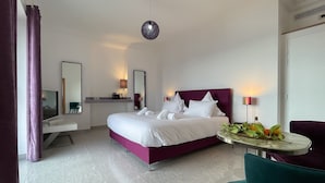 A modern hotel room with a large bed, a bedside table with a lamp, a TV, and a small table with fruit. - Exceptional panoramic view with beach and town on foot (Menton)