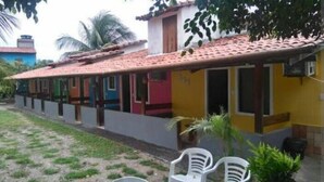 Una hilera de casas coloridas con techo de tejas, un área verde al frente y algunas sillas de plástico.