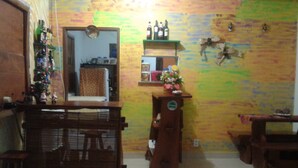 Una habitación con una mesa de comedor de madera, sillas, un pequeño armario de madera y una pared decorada con patrones coloridos y un reloj.
