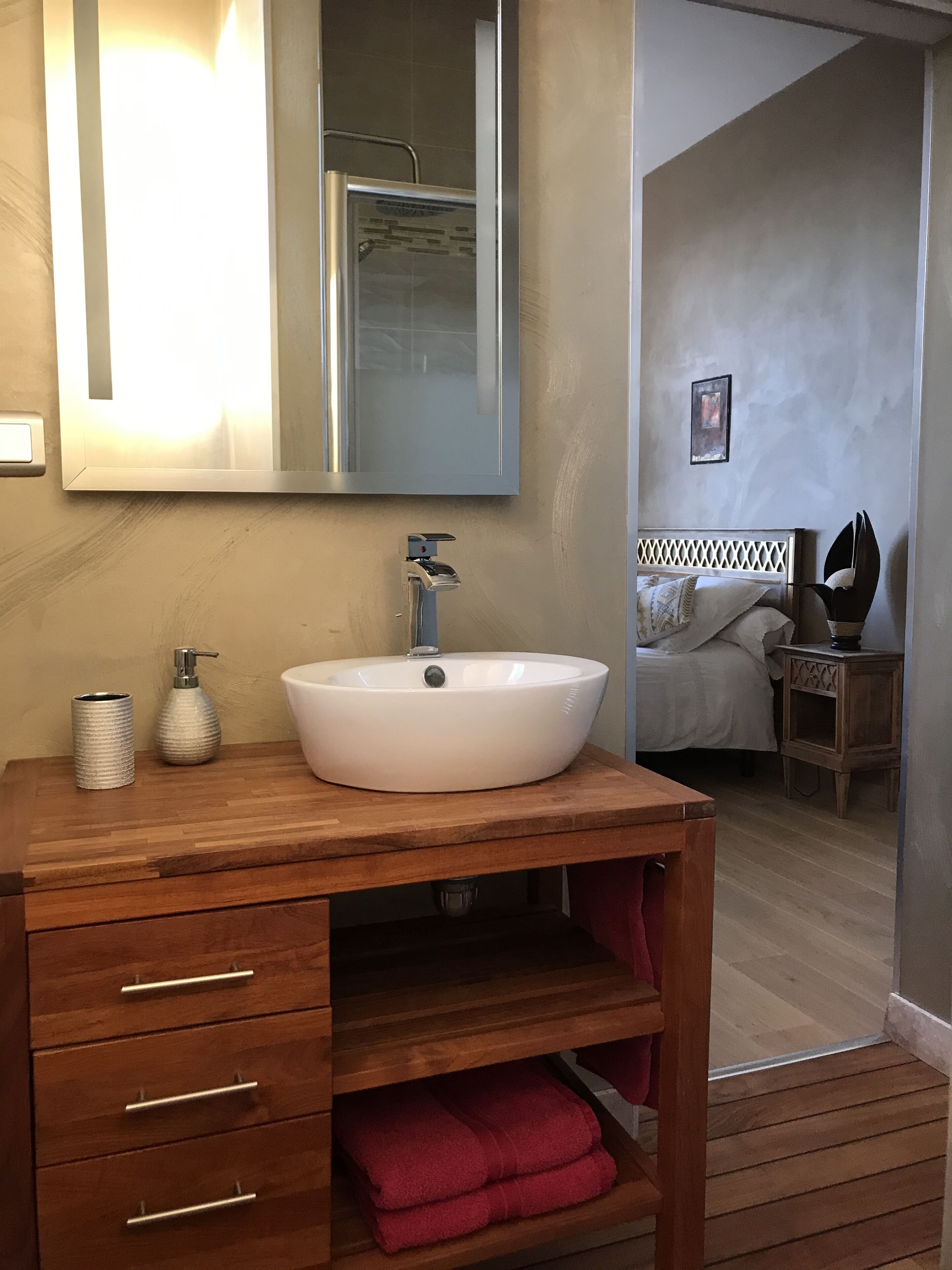 A bathroom with a wooden vanity, a white sink, a mirror, and a red towel.