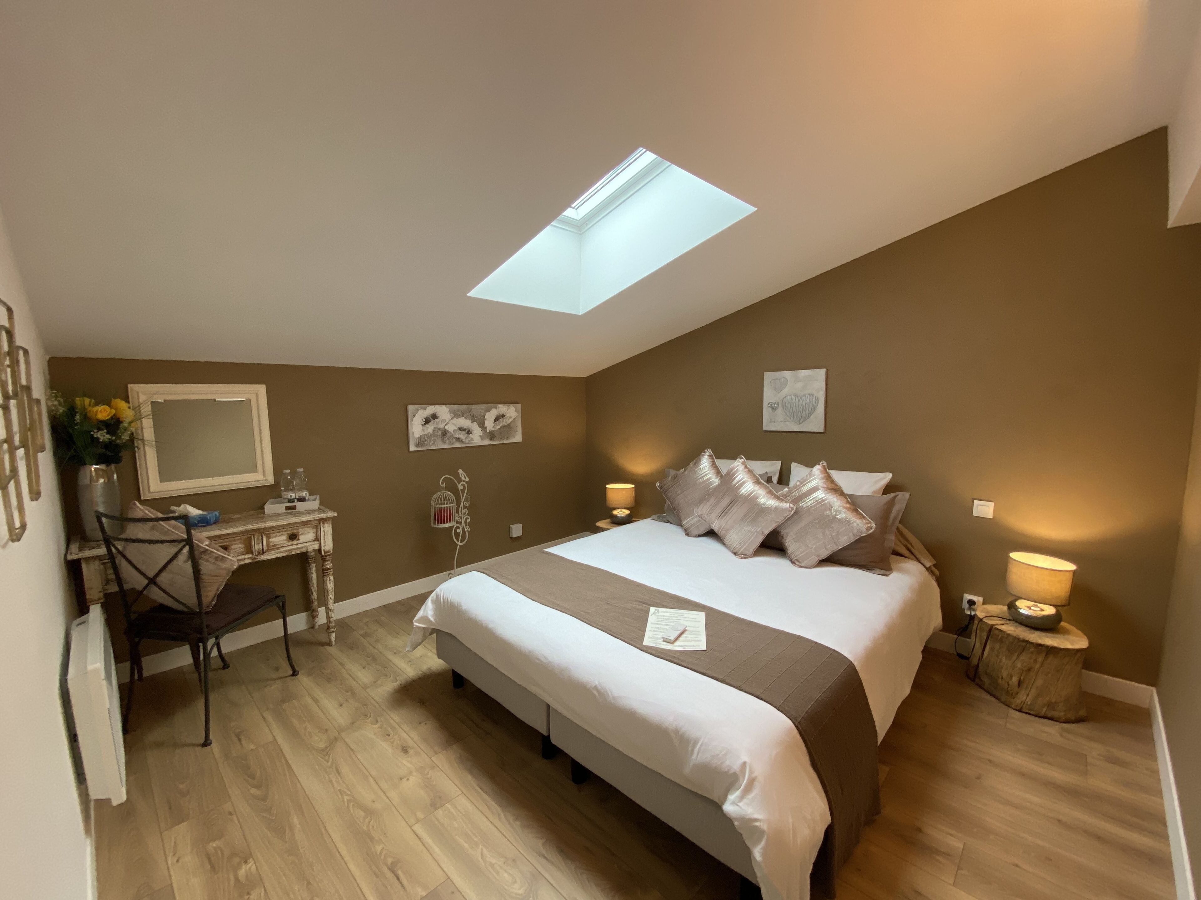 Ein Schlafzimmer mit Oberlicht, einem Bett mit vielen Kissen, einem Schreibtisch mit Spiegel und einem kleinen Nachttisch mit Lampe.