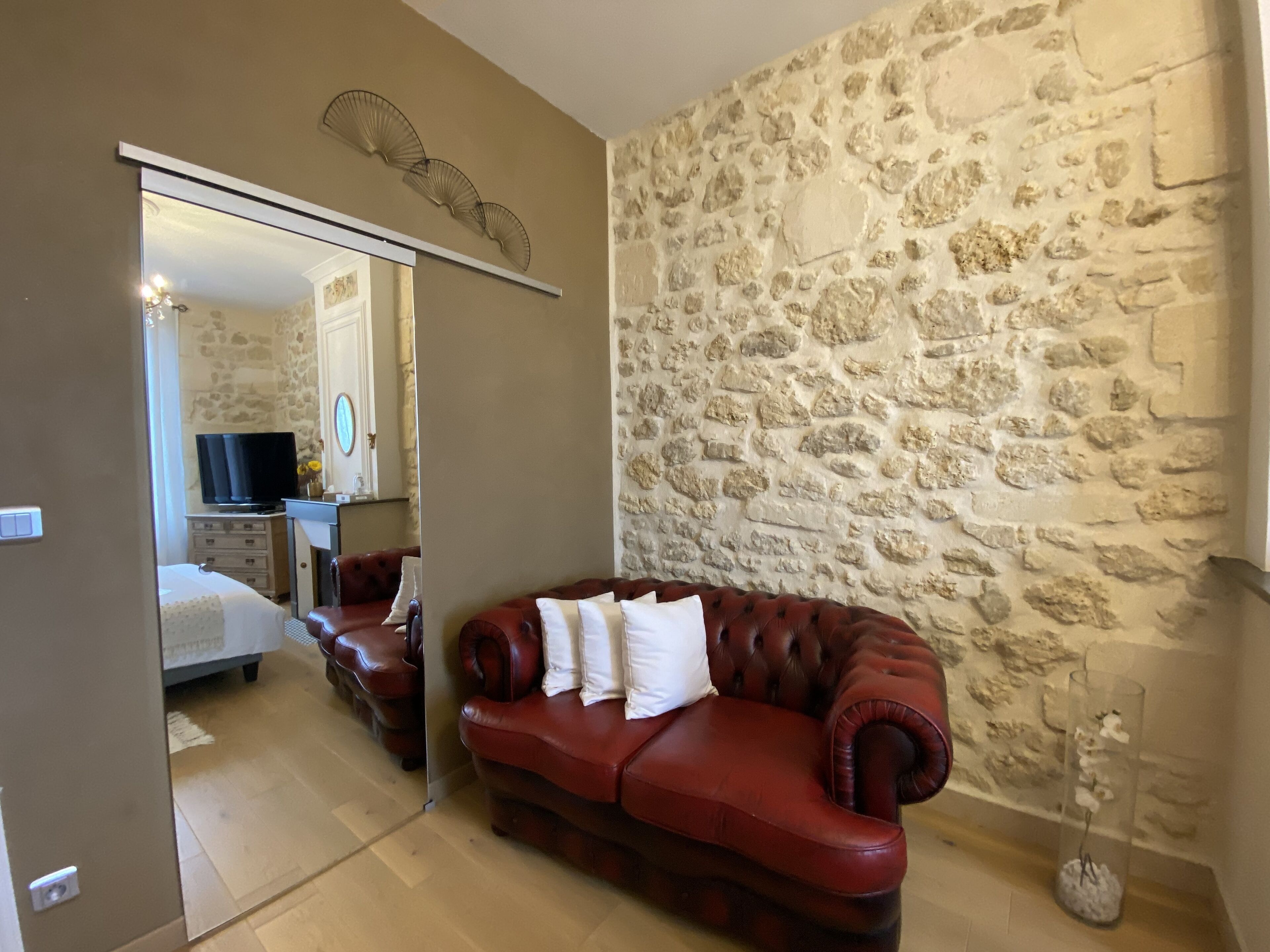 A room with a stone wall, a red leather sofa with pillows, a mirror, and a television in the background.