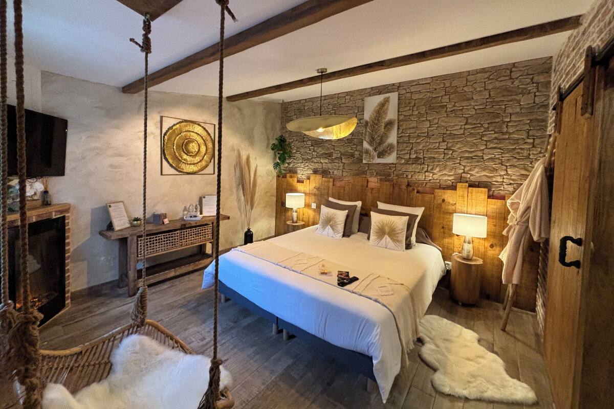 Ein Schlafzimmer mit einem großen Bett, einem Holzkopfende, einem Hängestuhl, einer Steinwand und einem Wand-Fernseher.