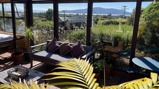 A sunlit patio with a seating area, potted plants, and a view of distant mountains and buildings.