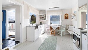 A compact kitchen with white cabinetry, a dining area with a table and chairs, and a view of mountains through the window. - Private Cozy House by the Fjord (Flakstad)