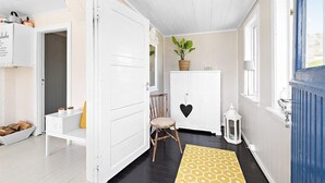 A hallway with a white door, a wooden chair, a white cabinet with a plant, and a yellow patterned rug. - Private Cozy House by the Fjord (Flakstad)