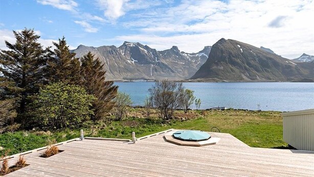 A wooden deck with a hot tub, overlooking a lake and mountains. - Private Cozy House by the Fjord (Flakstad)