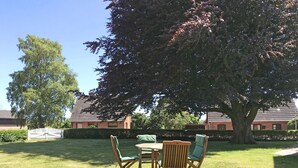 An outdoor seating area with a table and chairs, a large tree, and a building in the background. - "Schleistern" Vacation Rental in Kappeln (Kappeln)