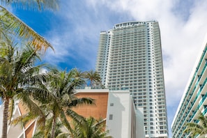 Un grand hôtel moderne, doté d’une façade incurvée et de nombreux balcons, entouré de palmiers et baigné par un ciel dégagé.