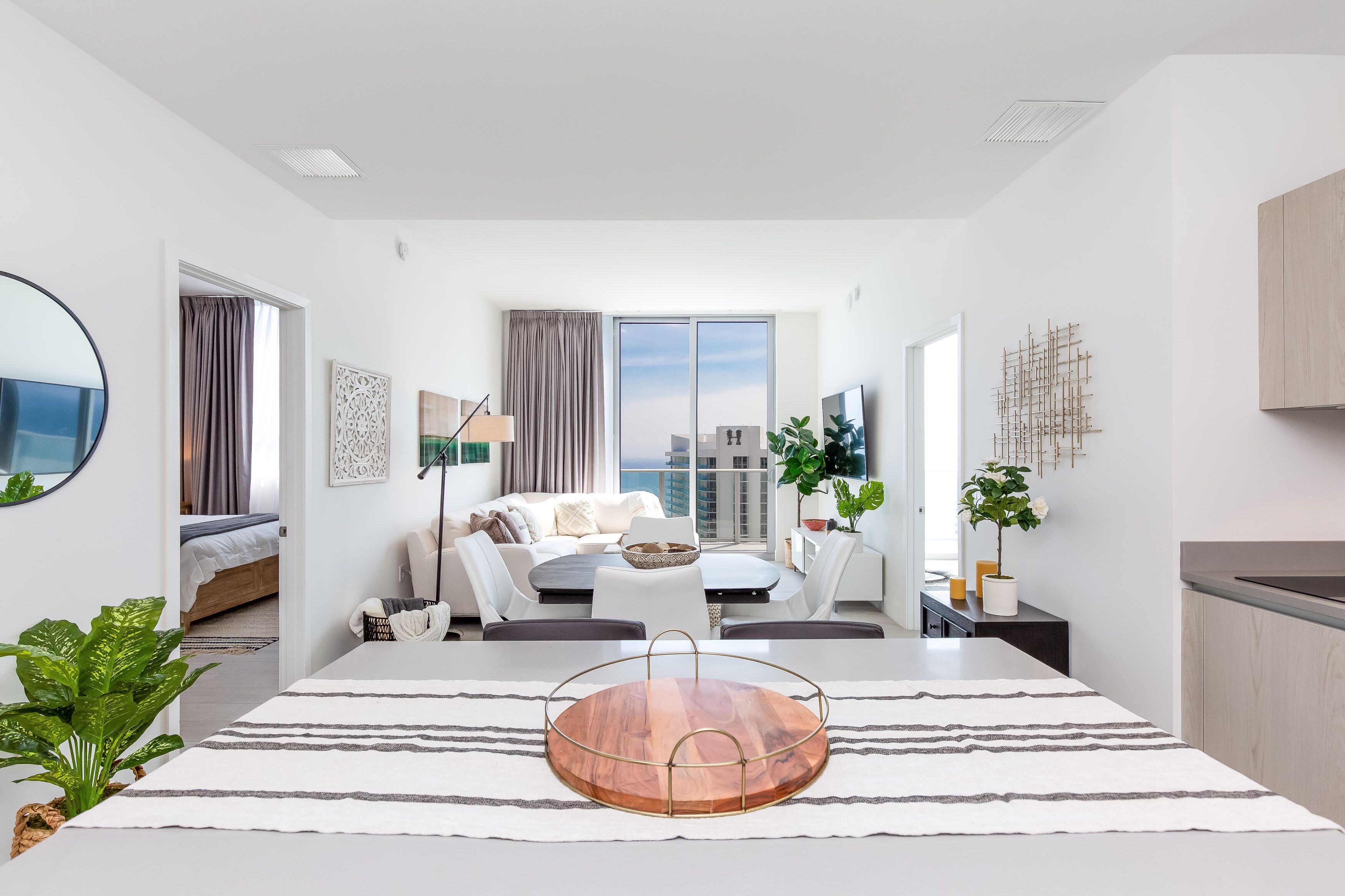A modern, well-lit living room with a sofa, coffee table, and a dining area with a wooden table.