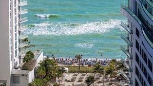 Un hôtel situé en bord de mer, doté de balcons avec vue sur l’océan, d’une plage de sable et de palmiers.