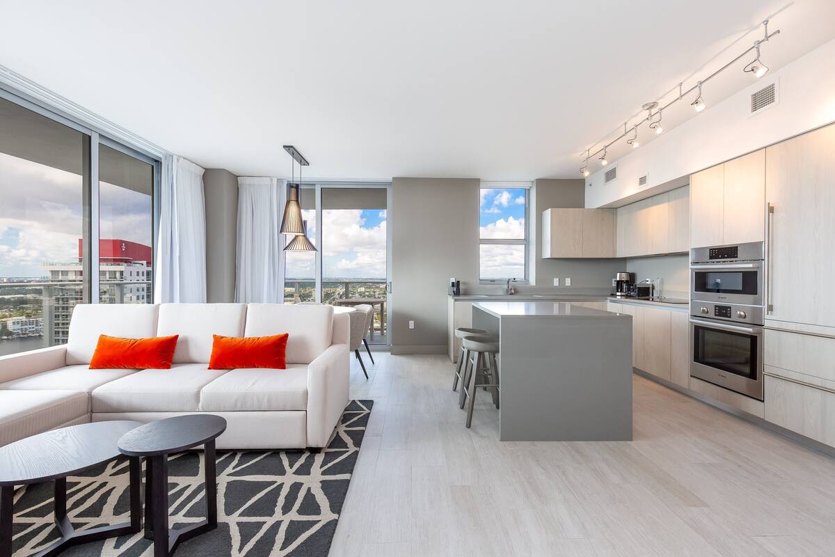 Eine moderne Wohnung mit Wohnbereich, Küche und großen Fenstern mit Blick auf die Stadt.