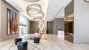 Un hall d’entrée spacieux au design moderne, agrémenté d’un grand tableau abstrait, de plusieurs espaces de détente et d’un luminaire au plafond original.