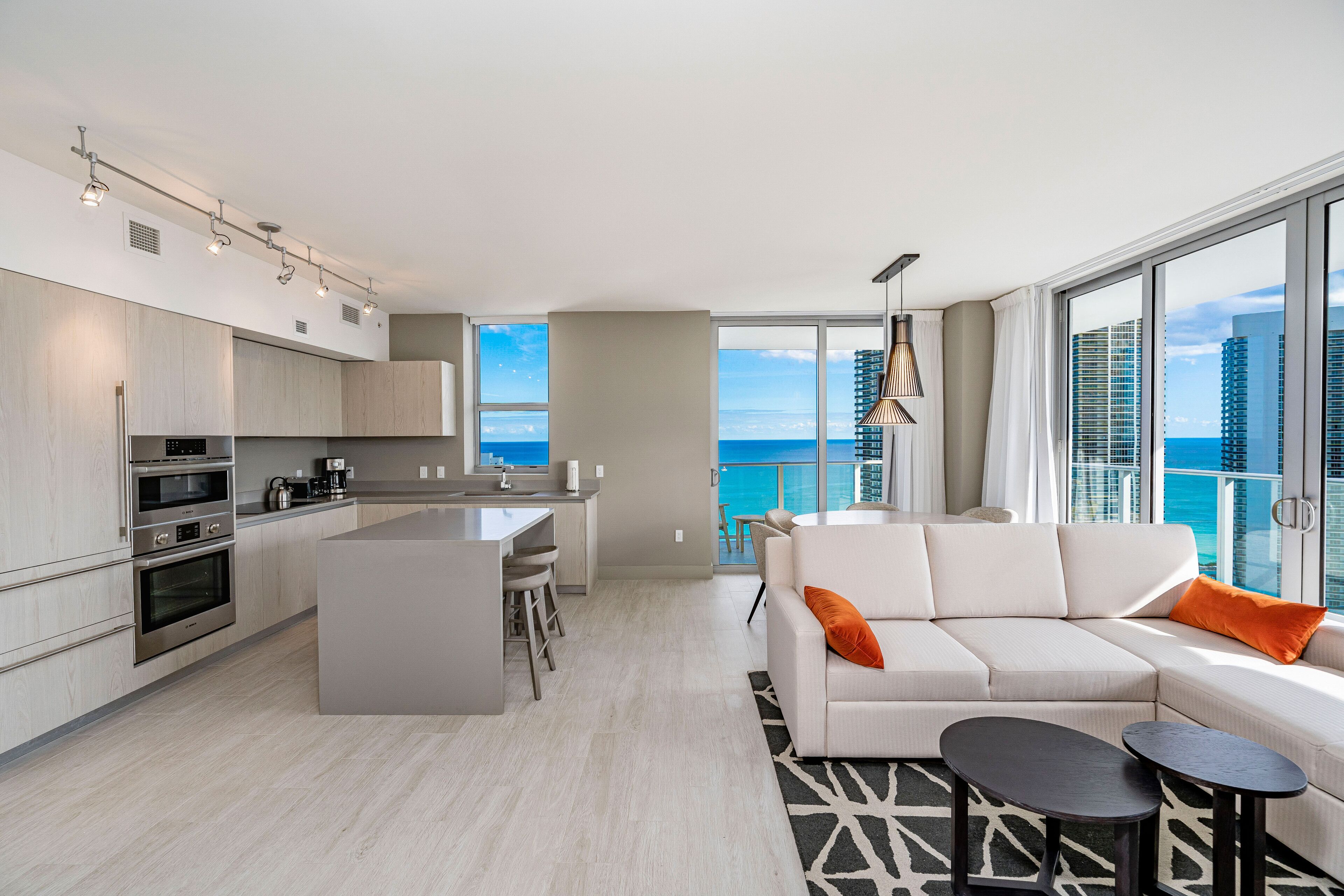 A modern kitchen with built-in appliances, a dining area, and a living room with a view of the ocean.