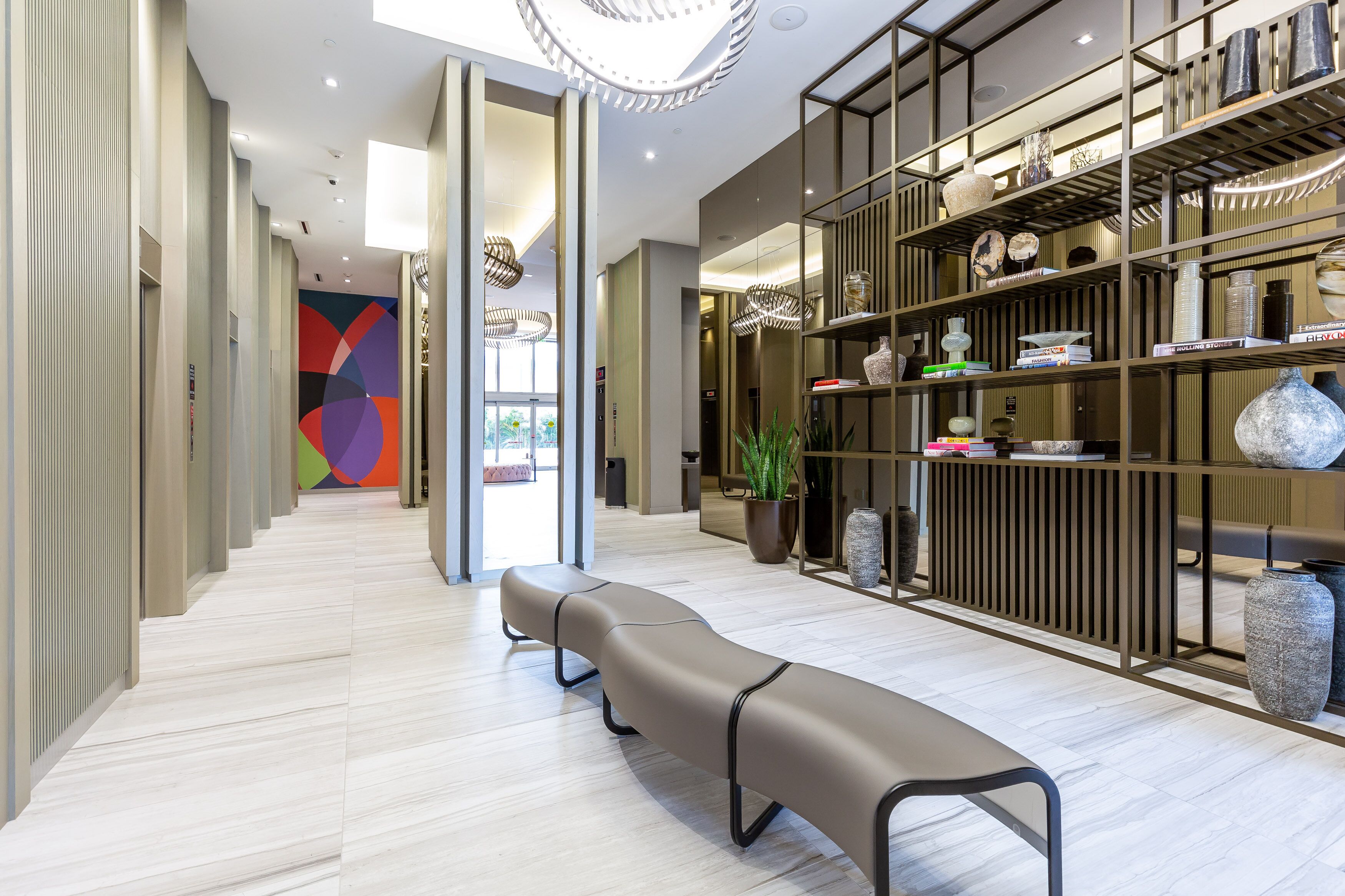 Eine moderne Hotelhalle mit einer langen Bank, einer farbenfrohen abstrakten Wand und einem ordentlich bestellten Bücherregal.