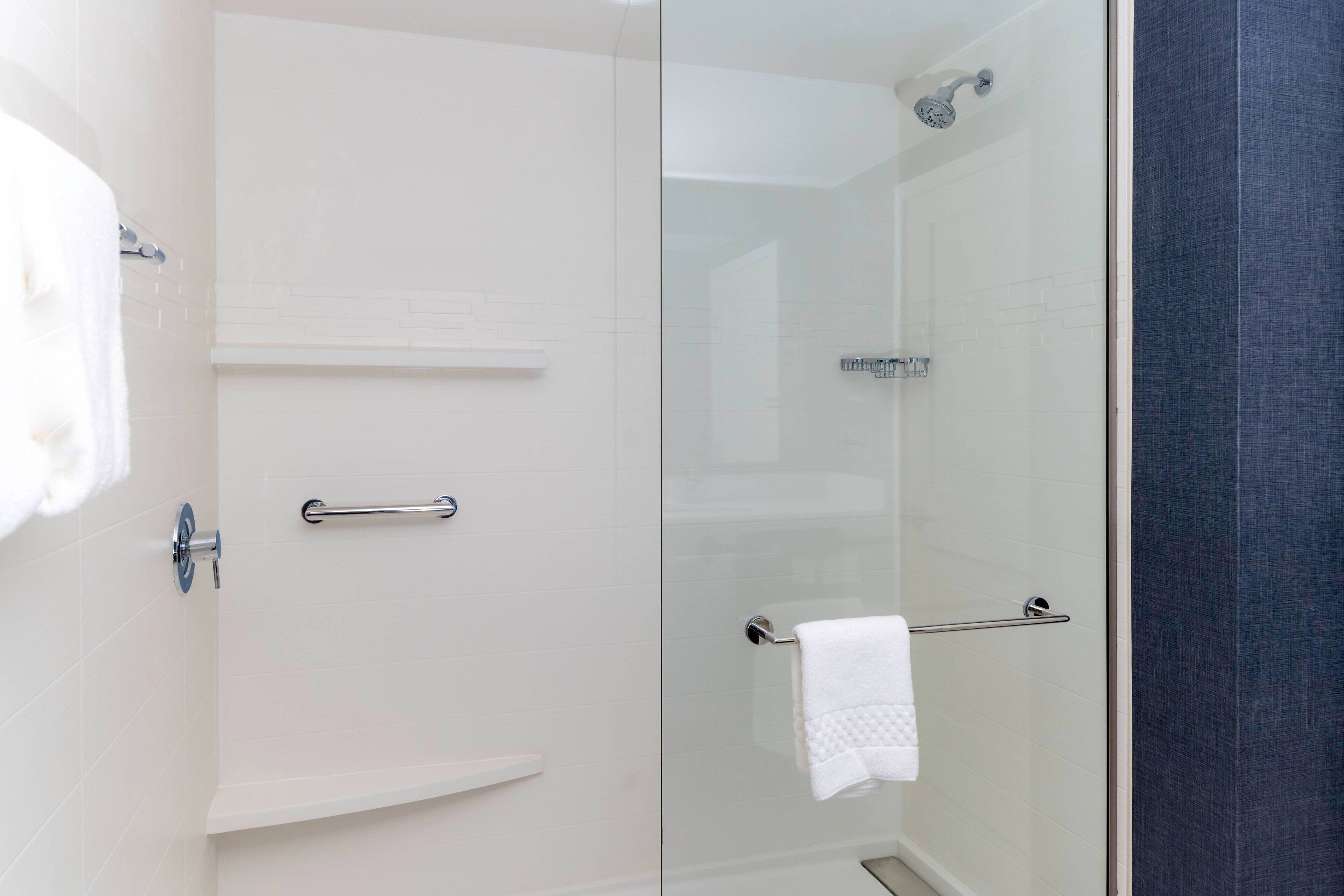 Un baño moderno con mampara de vidrio, un perchero blanco y una toalla blanca colgada.