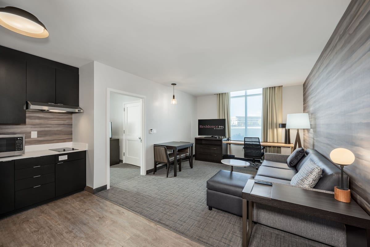 Een moderne hotelkamer met een keuken, eethoek en een bank met een lamp.