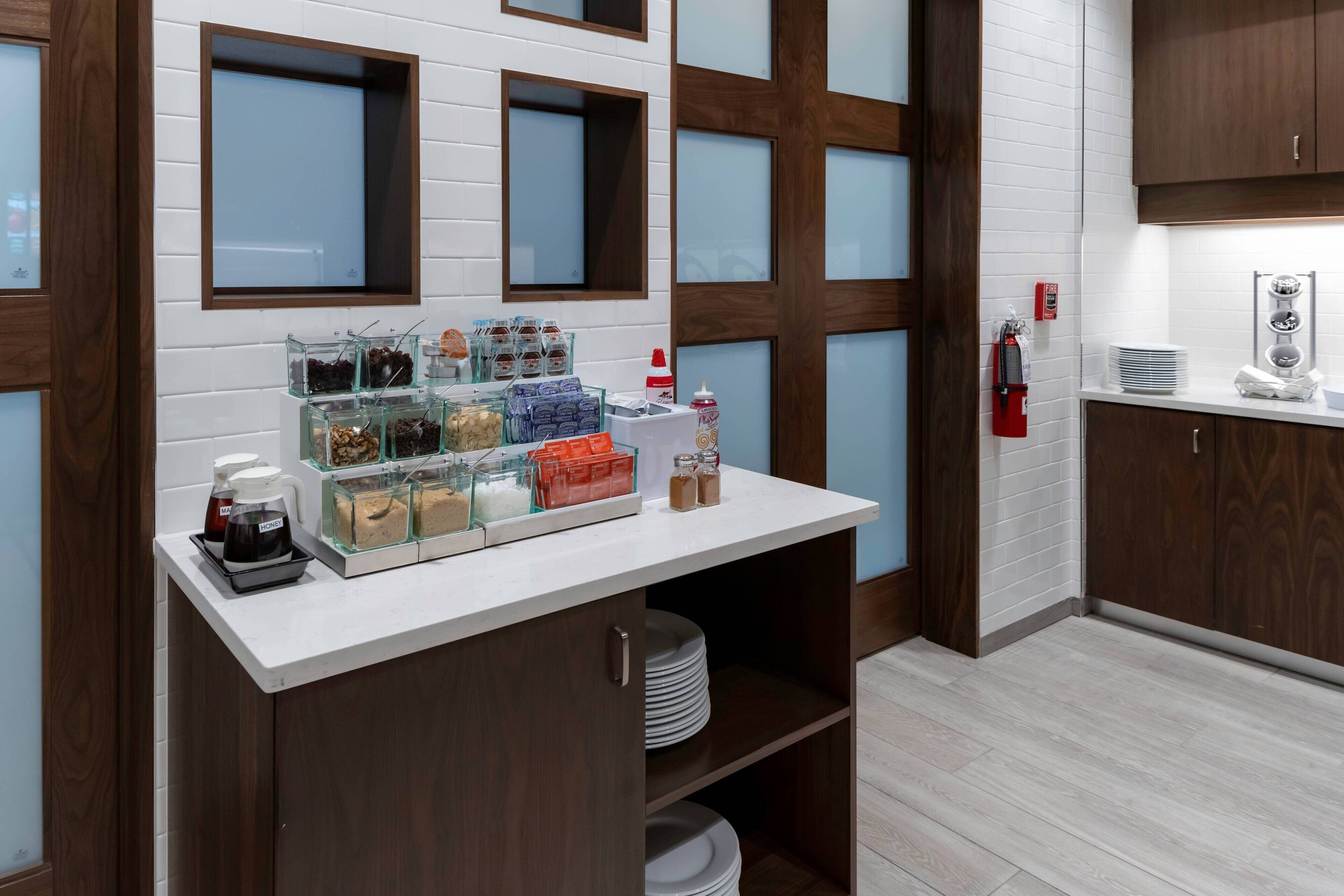 Una kitchenette con encimera blanca, recipientes de vidrio y cafetera.