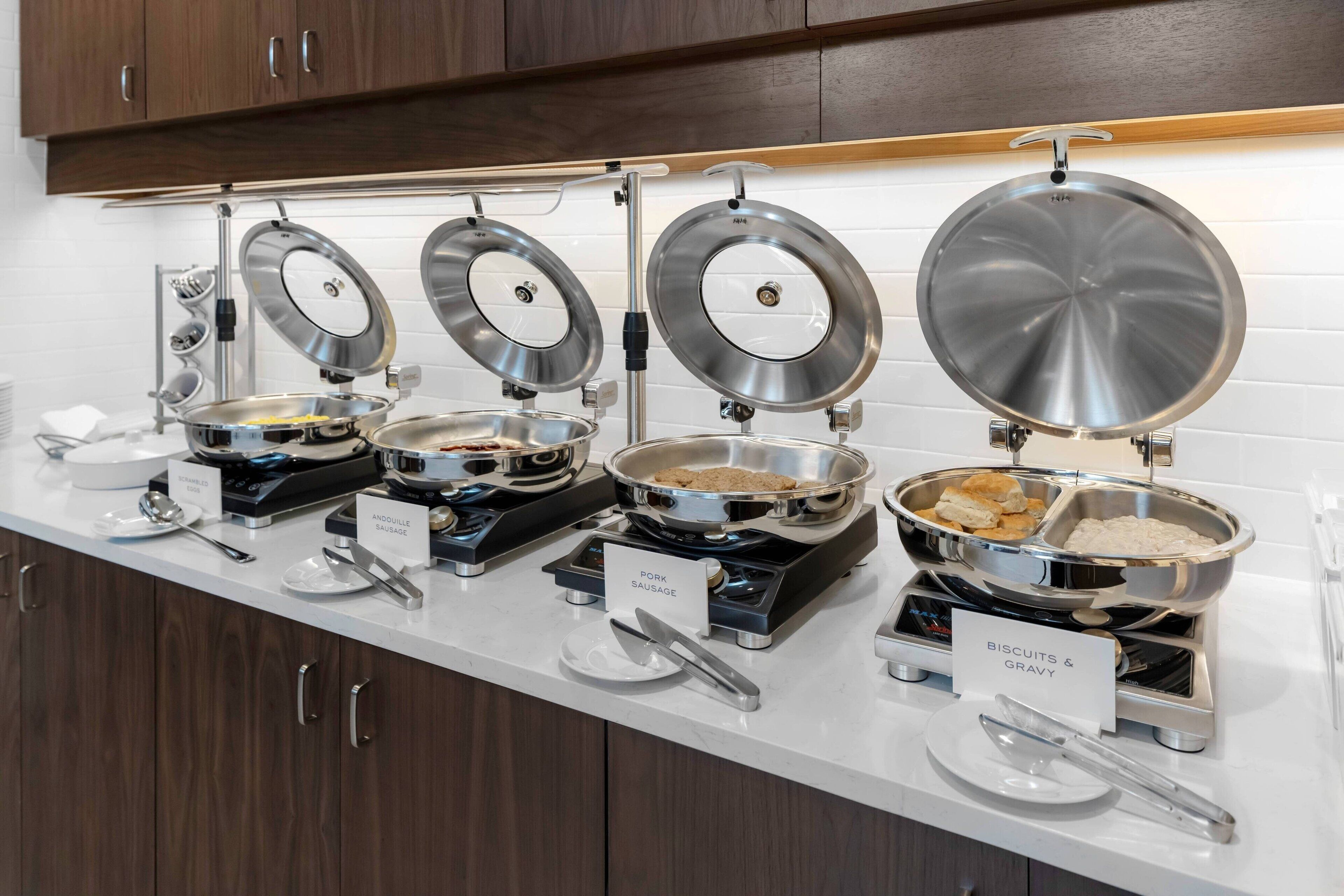 A buffet setup with various food stations including pork sausage, biscuits & gravy, and other dishes.