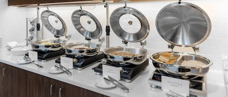 A buffet setup with various food stations including pork sausage, biscuits & gravy, and other dishes.