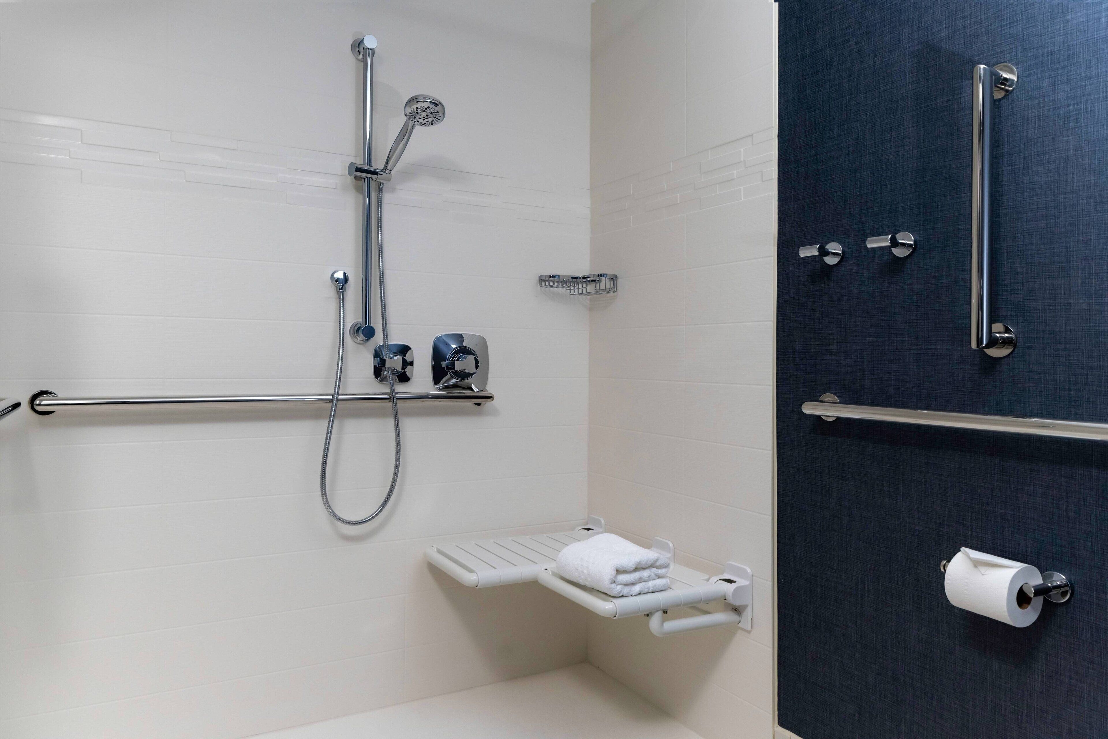 A bathroom with a shower, grab bars, a towel rack, and a toilet paper holder.